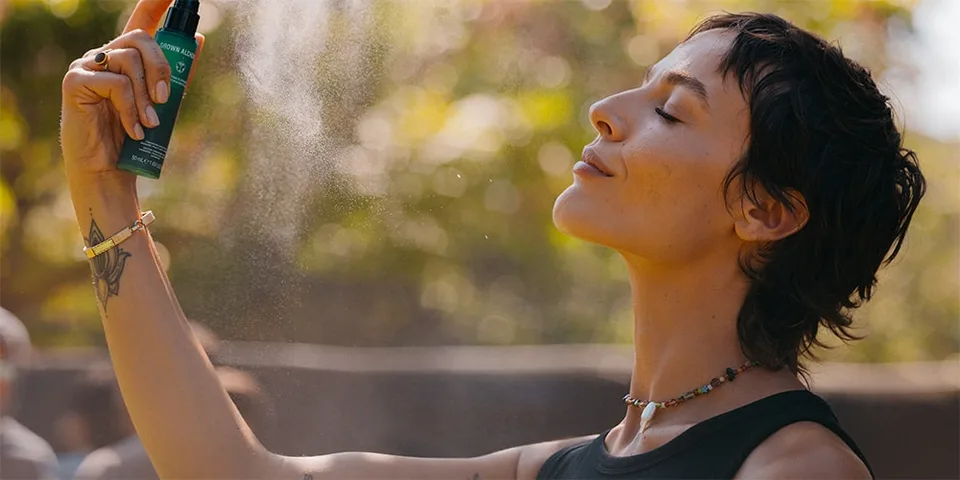Personne vaporisant son visage avec un produit de soin dans la nature.