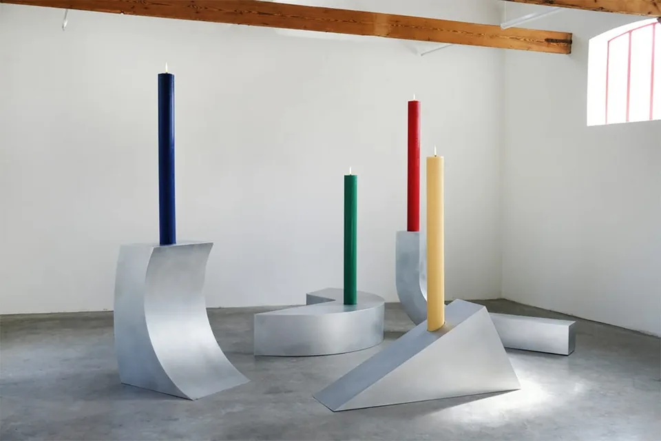 Quatre bougies colorées sur des structures métalliques géométriques dans une salle.