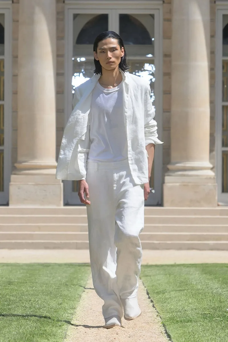 Homme défilant en tenue blanche élégante devant bâtiment classique.