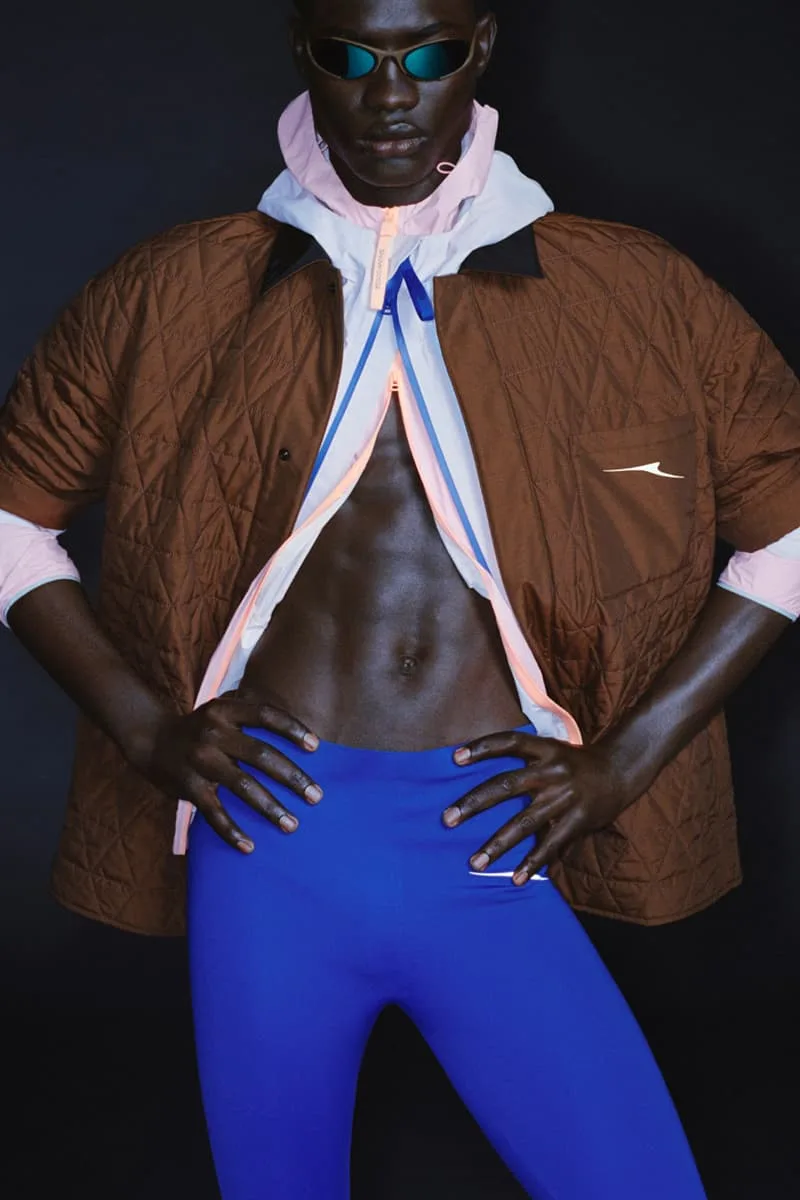 Personne avec des lunettes de soleil, veste matelassée et leggings bleus sur fond noir.