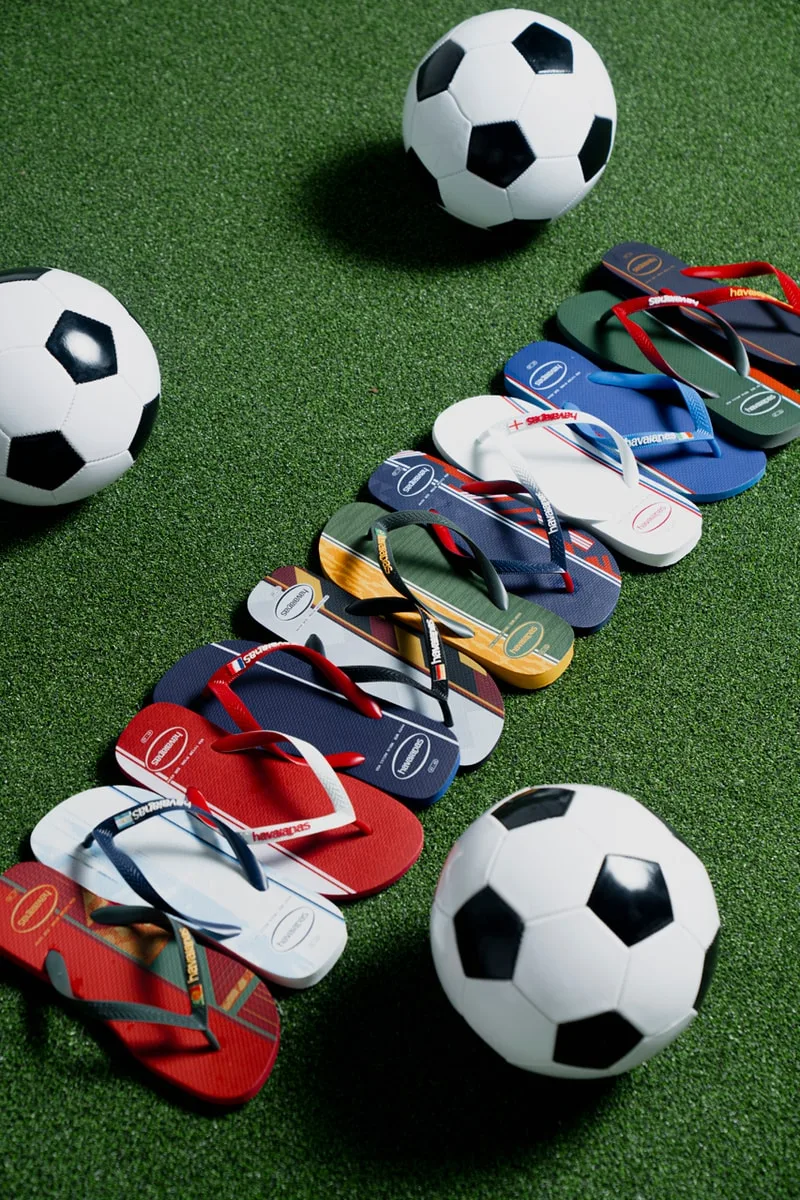 Tongs colorées alignées sur gazon avec ballons de football.