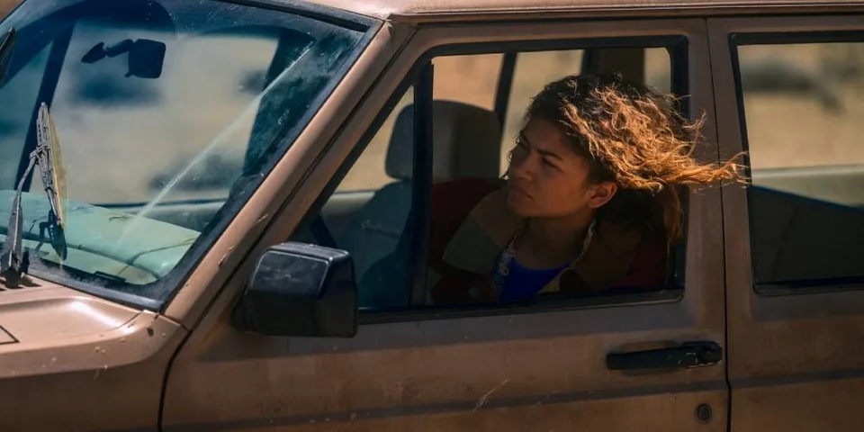Femme conduisant une voiture marron dans un paysage désertique.
