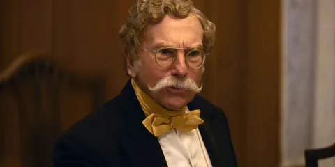 Homme moustachu en costume avec lunettes rondes et nœud papillon jaune.