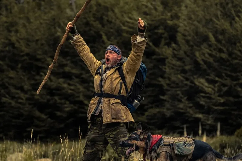 Un homme lève un bâton avec un chien dans la nature.