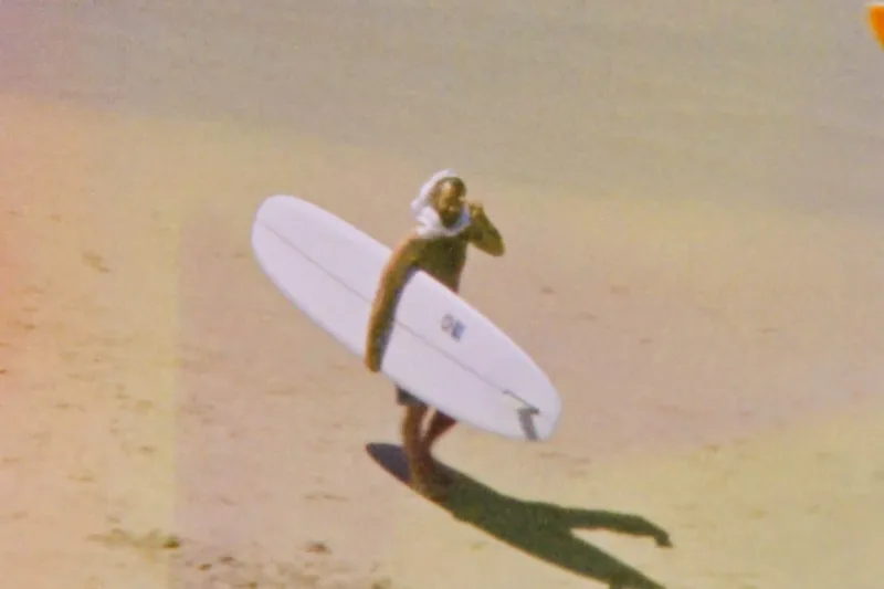 Une personne portant une planche de surf sur une plage.