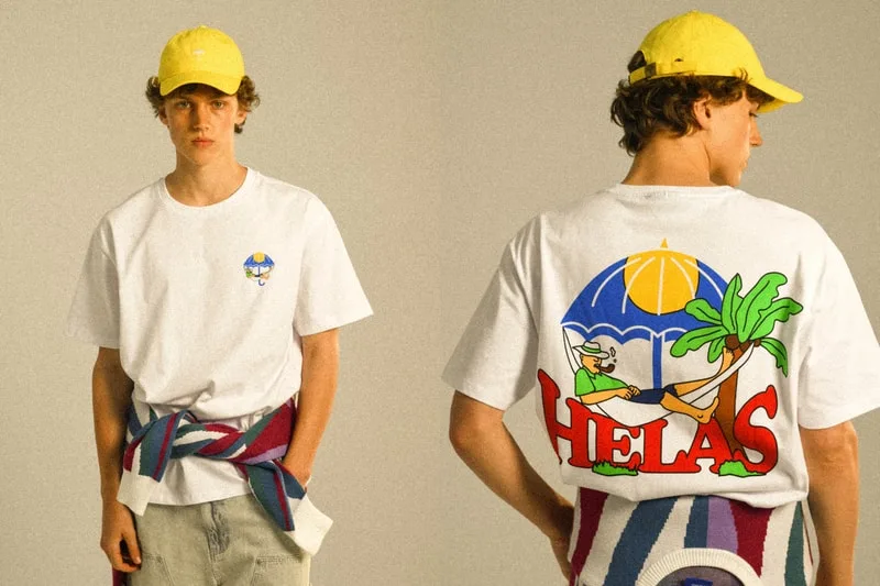 Jeune homme avec casquette jaune, t-shirt motif Helas, et pull à rayures à la taille.