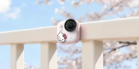 Caméra avec design Hello Kitty sur une balustrade, arrière-plan flou avec fleurs de cerisier.