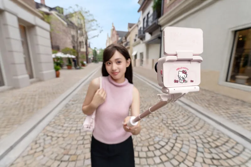 Femme tenant un selfie stick sur une rue pavée.