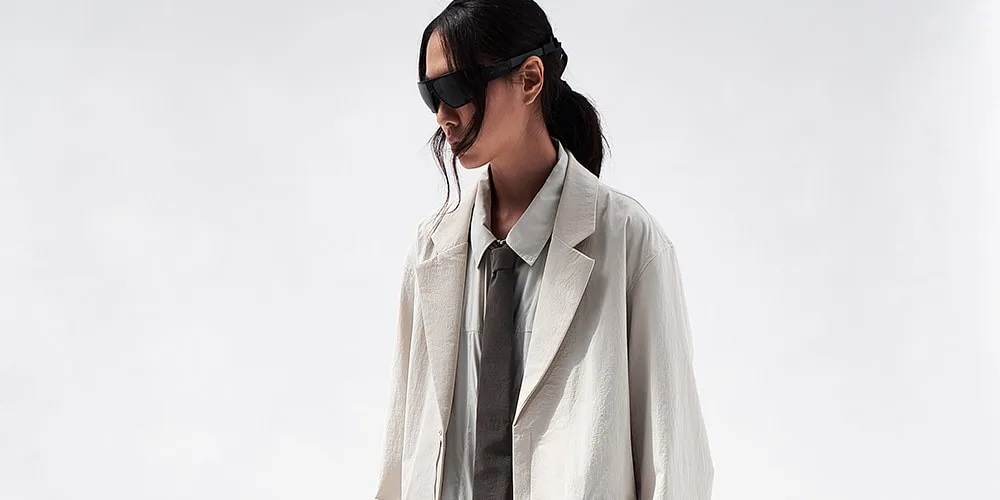 Personne en manteau élégant et lunettes de soleil, fond clair.