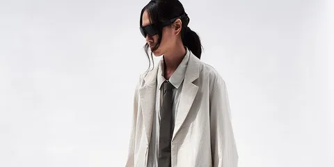 Personne en manteau élégant et lunettes de soleil, fond clair.