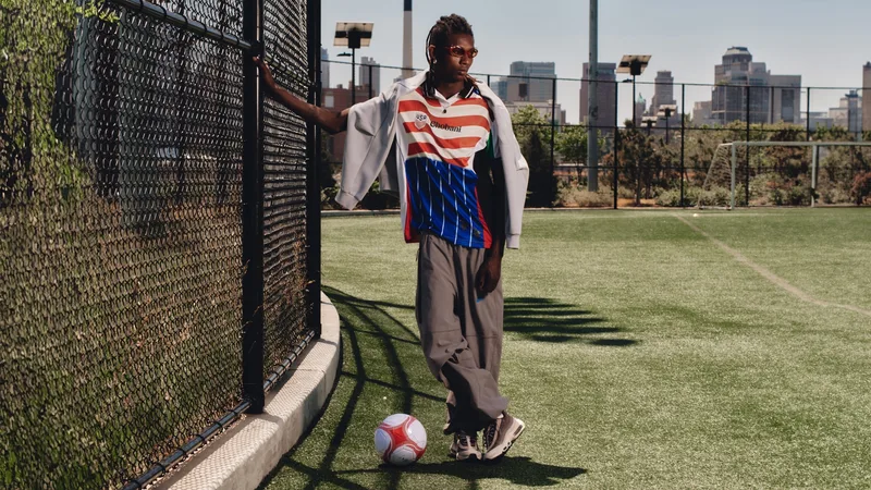 Personne mode posant sur un terrain de football avec un ballon, fond urbain.