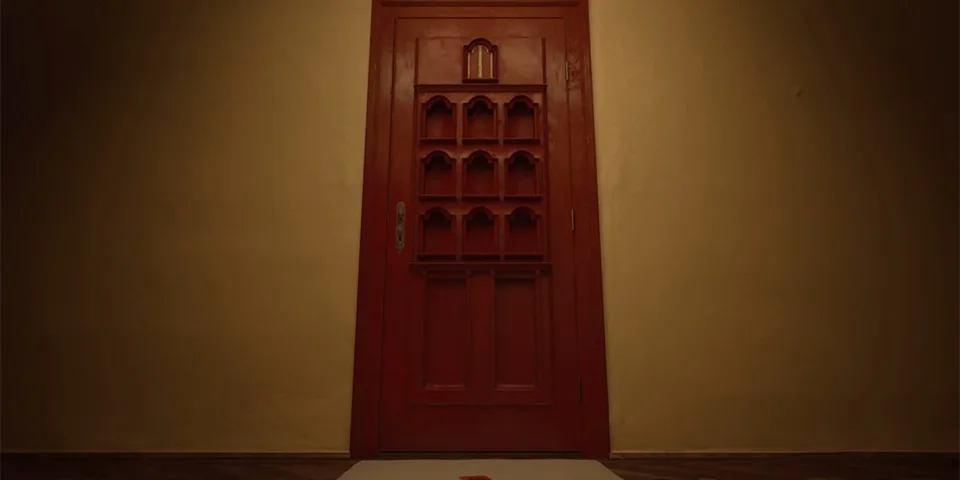 Porte rouge en bois dans une pièce sombre avec lumière tamisée.