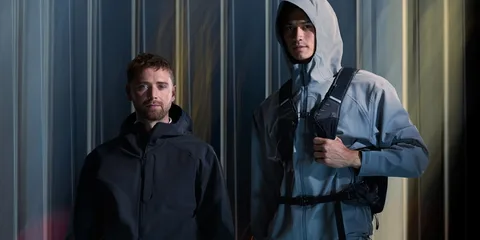 Deux hommes en vestes techniques devant un fond métallique.