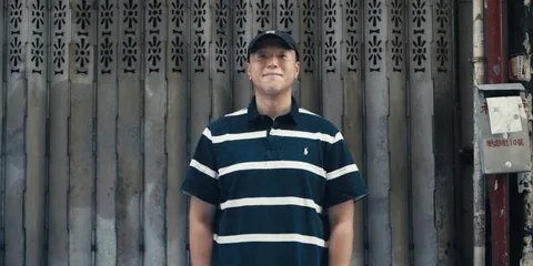 Homme souriant avec polo rayé devant un rideau métallique.