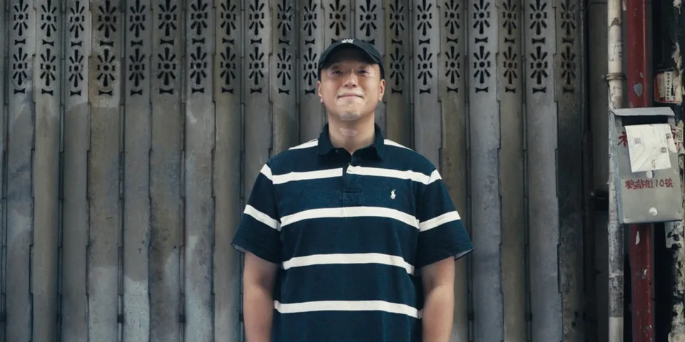 Homme souriant avec polo rayé devant un rideau métallique.