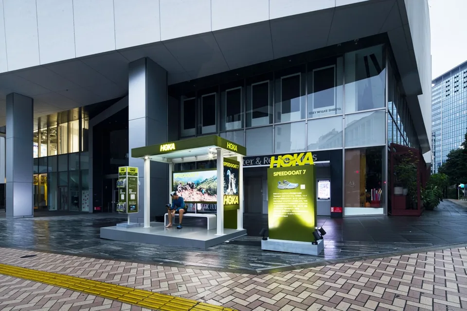 Kiosque HOKA moderne avec un écran et un homme assis dans un environnement urbain.