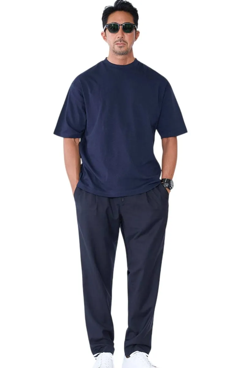 Homme portant un t-shirt et un pantalon bleu marine avec des lunettes de soleil.