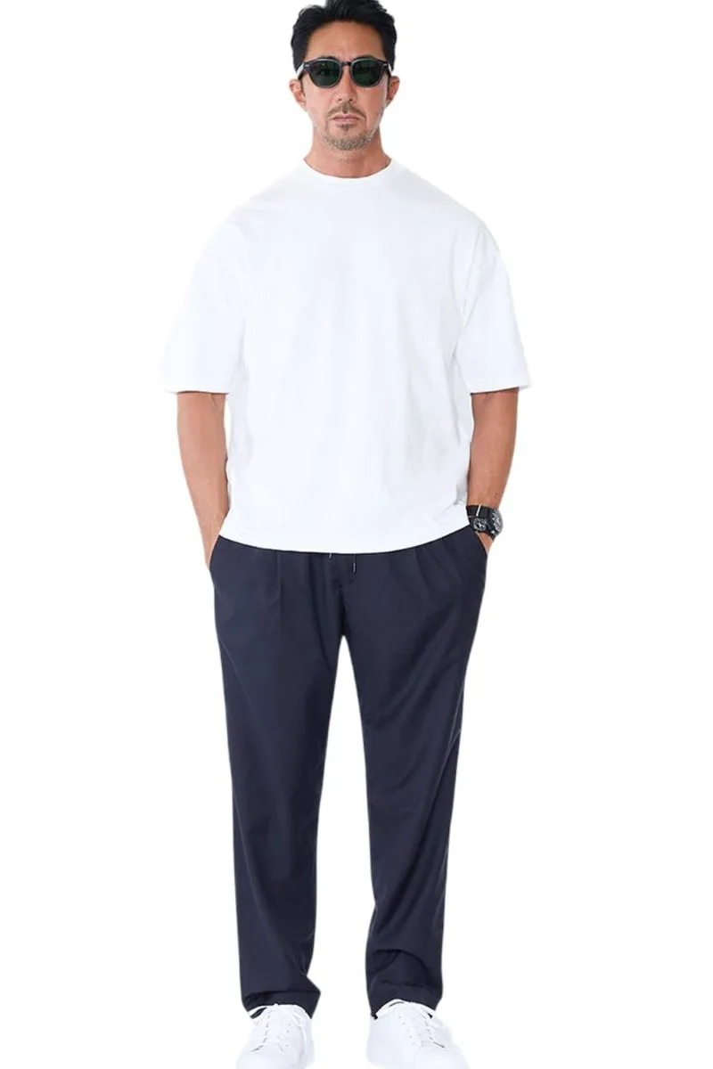 Homme en t-shirt blanc et pantalon noir, portant des lunettes de soleil.