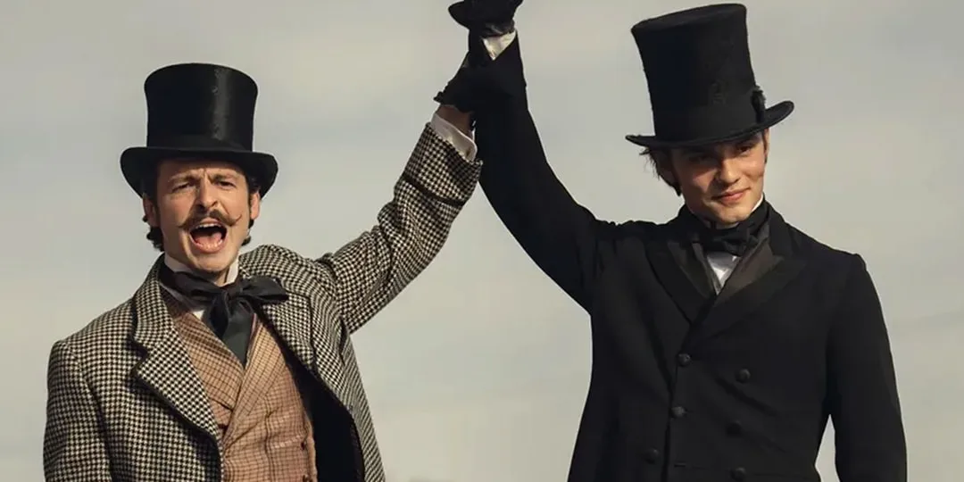 Deux hommes en chapeaux hauts se tenant la main souriants.