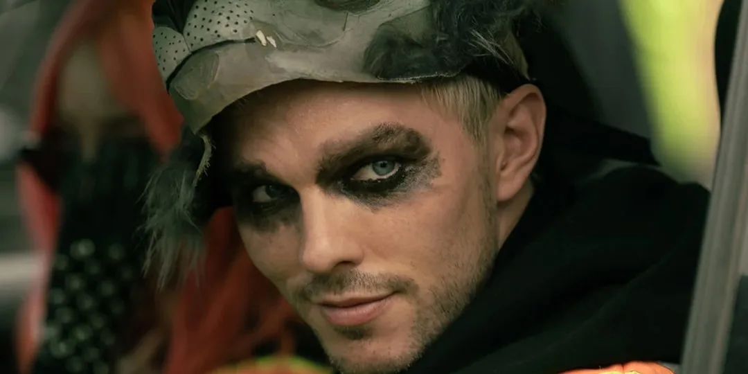 Homme avec maquillage intense et masque, regard confiant, style post-apocalyptique.