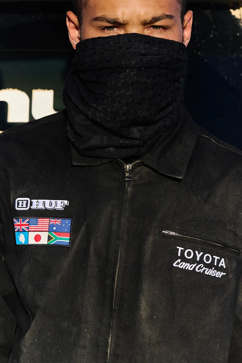 Homme en veste avec logos et écharpe couvrant le visage, extérieur.