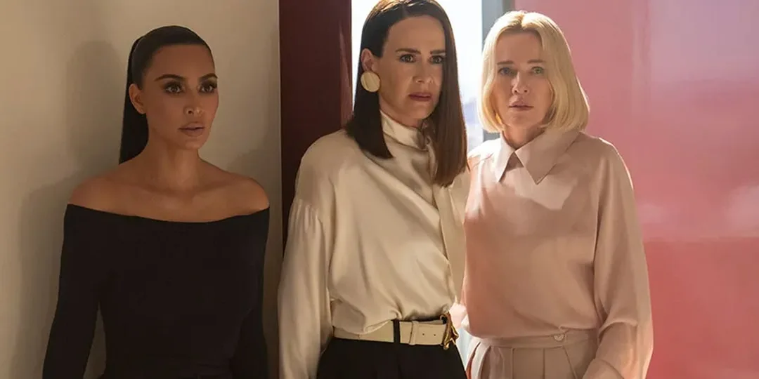 Trois femmes debout contre un mur de couleur crème et rose.