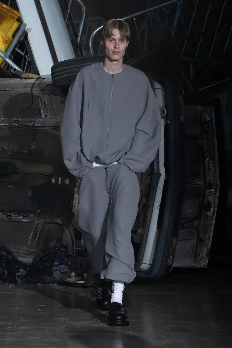 Modèle en tenue grise défilant sur un fond industriel.