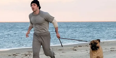 Homme courant sur la plage avec un chien en laisse.