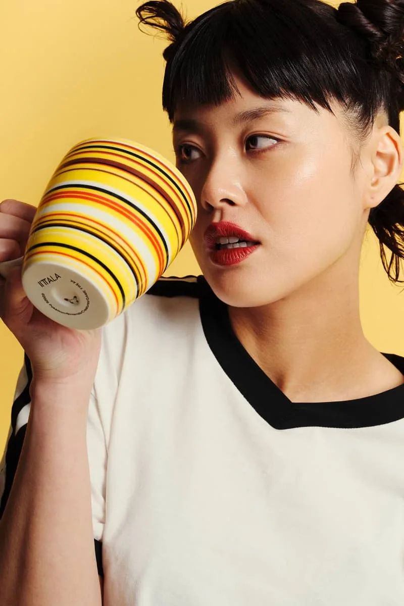 Femme tenant une grande tasse rayée sur fond jaune.