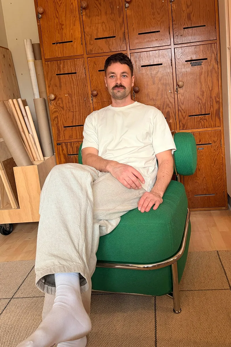 Homme assis sur une chaise verte devant de grands tiroirs en bois.