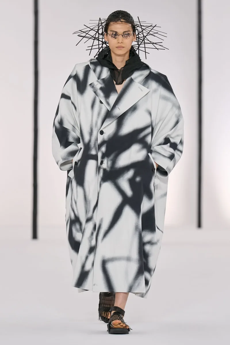 Modèle porte un manteau ample à motifs noirs et blancs sur une piste de défilé.