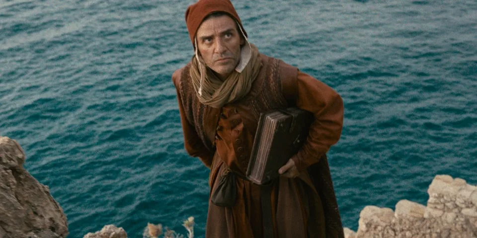 Homme en costume médiéval tenant une mallette devant la mer.