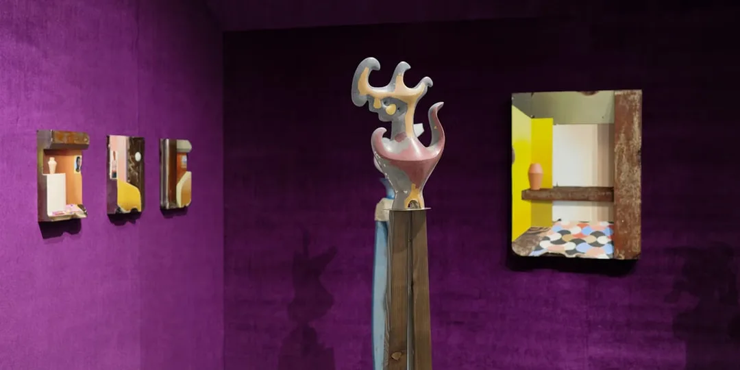 Galerie d'art avec sculptures et miroirs sur murs violets.
