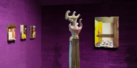 Galerie d'art avec sculptures et miroirs sur murs violets.