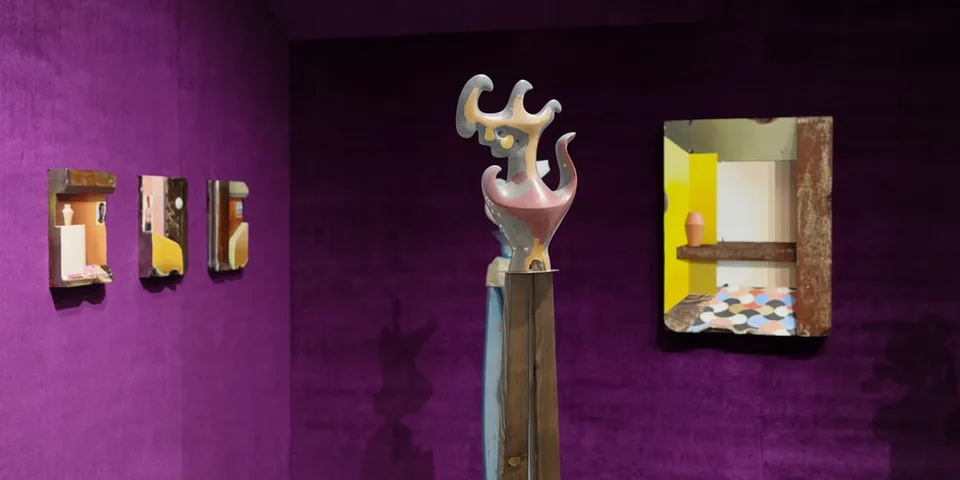 Galerie d'art avec sculptures et miroirs sur murs violets.