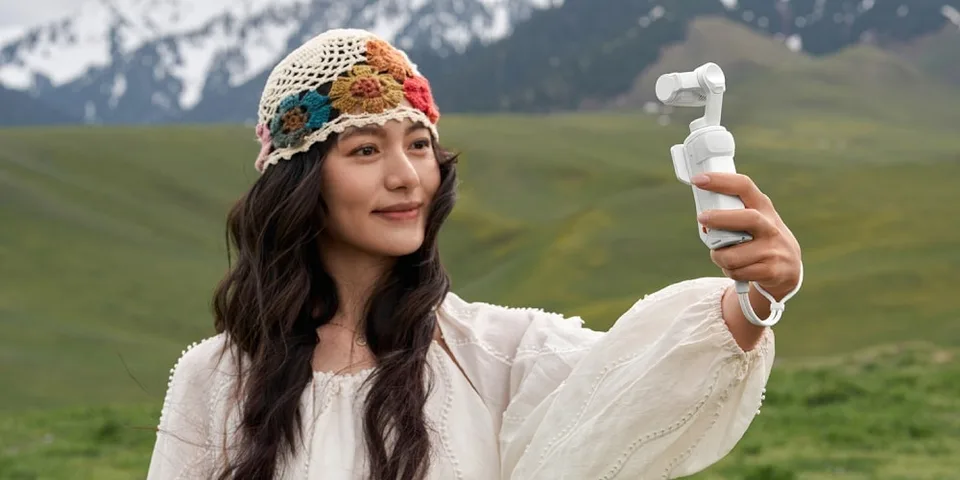 Femme avec chapeau et caméra dans un paysage montagneux.