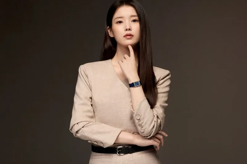 Femme en blazer beige avec montre bleue, fond sombre.