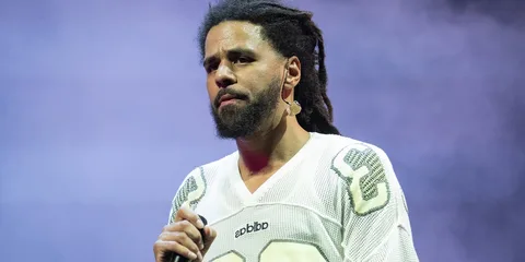 Homme avec micro, cheveux rasta, sur scène.
