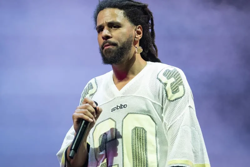 Homme avec dreadlocks et micro sur scène, chemise sportive.