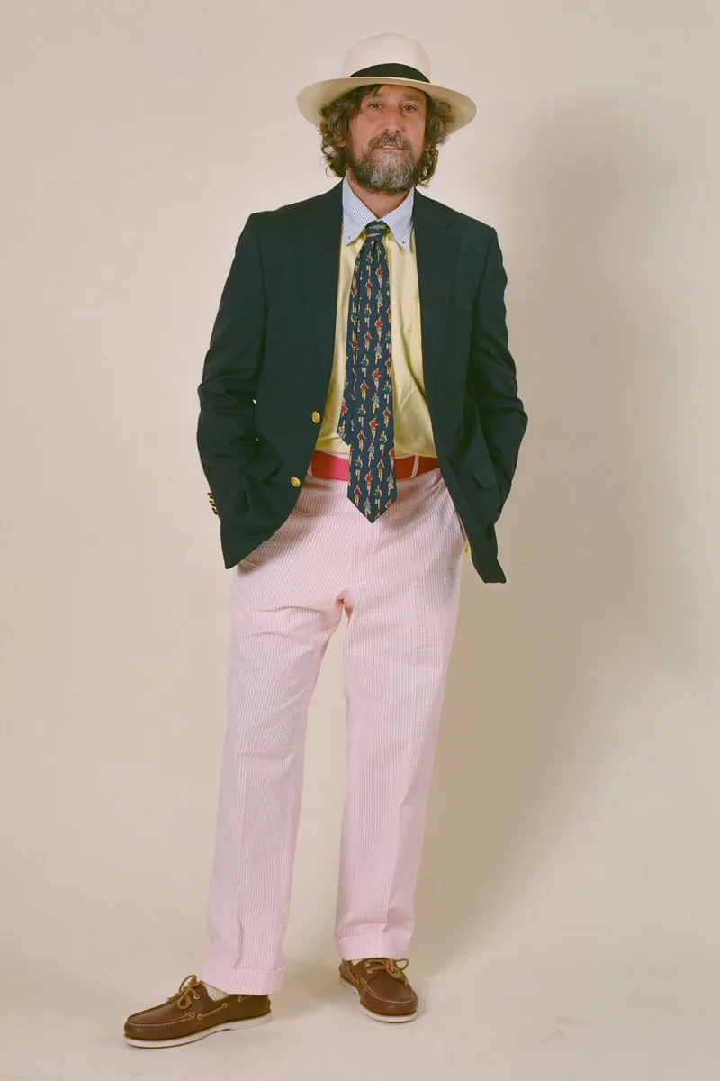 Homme en costume coloré avec chapeau et cravate, debout en pose décontractée.