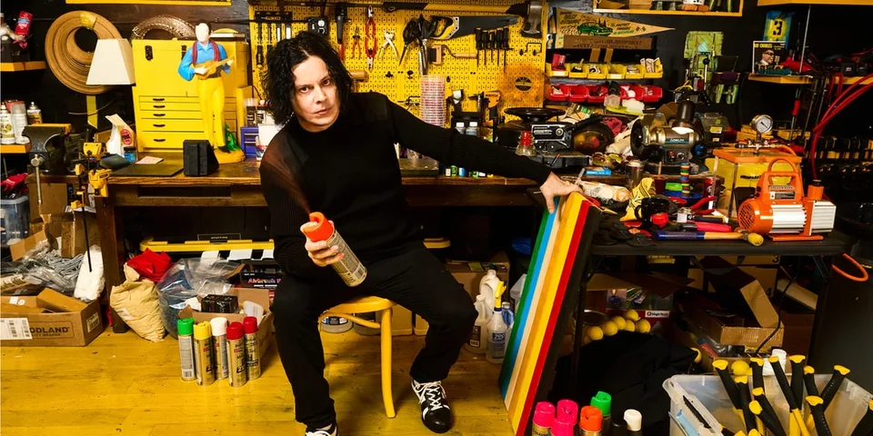 Homme assis dans un atelier rempli d'outils et de peinture colorée.