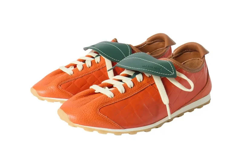 Chaussures orange avec languette verte et lacets beiges sur fond blanc.