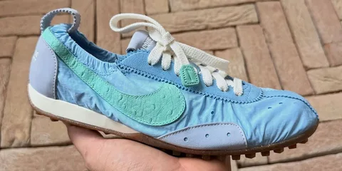 Chaussure de sport bleue avec logo vert sur fond de pavés.