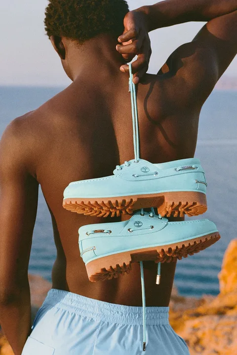 Homme tenant des chaussures bleu ciel devant une mer.