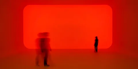 Salle lumineuse rouge avec silhouettes floues de personnes.