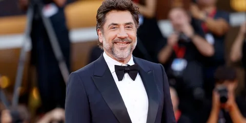 Homme en smoking sur un tapis rouge, souriant.