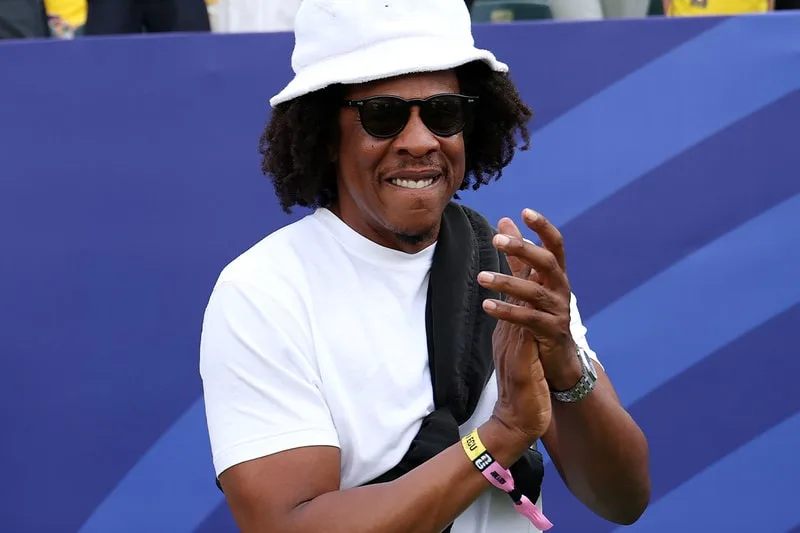 Homme avec chapeau blanc et lunettes noires applaudissant.