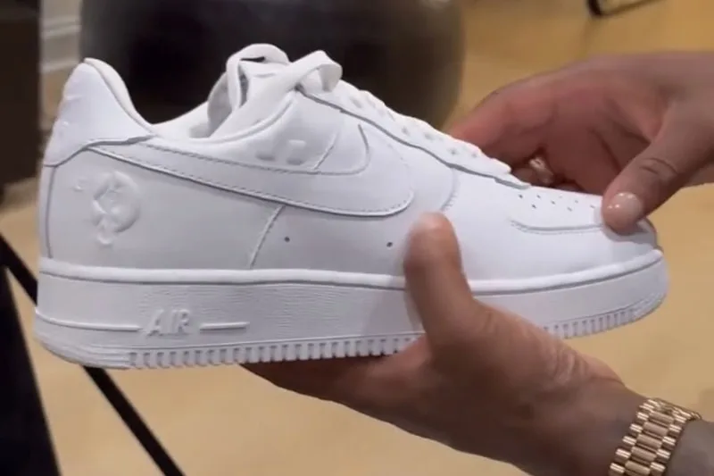 Main tenant une chaussure blanche avec un logo Nike.