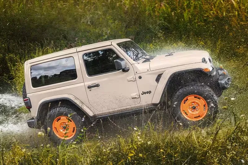 Jeep beige avec roues orange traverse un champ d'herbe.