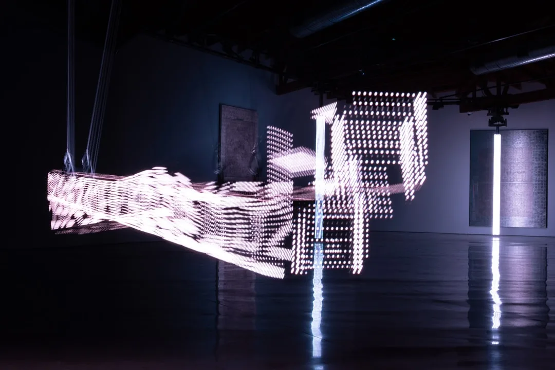 Installation lumineuse abstraite dans une galerie sombre.